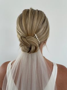 a woman with blonde hair wearing a white veil and pearls in her hair is seen from the back