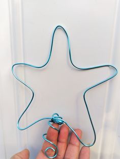 a hand holding a wire wrapped star shaped object in front of a white wall with a blue string attached to it