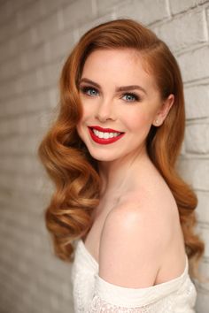 a woman with red hair and blue eyes posing for a photo in front of a brick wall