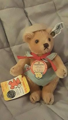 a brown teddy bear sitting on top of a bed with a tag in it's ear