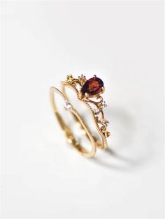 two gold rings with garnets and diamonds on the sides, one has a red stone