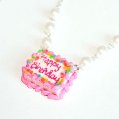 a pink birthday cake with sprinkles and pearls on a white necklace that says happy birthday