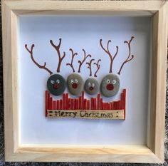 three rocks in a frame with reindeer faces on them, and the words merry christmas