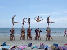 a group of people standing on top of each other in front of the ocean with their hands up