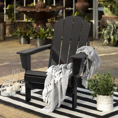 a black adirondack chair sitting on top of a striped rug next to potted plants