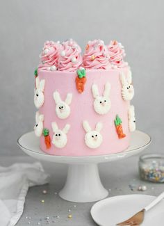 a pink cake decorated with bunnies and carrots on a white plate next to a fork