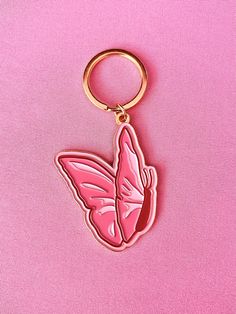 a pink butterfly shaped keychain sitting on top of a pink surface