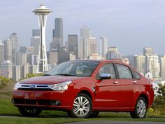 a red car is parked in front of a cityscape and the space needle