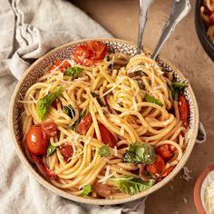 a bowl of pasta with tomatoes, basil and parmesan cheese on the side