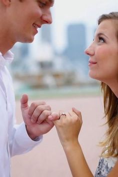 a man and woman holding hands while standing next to each other in front of a cityscape