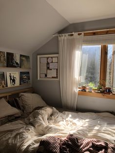 an unmade bed sitting under a window next to a wooden shelf with pictures on it