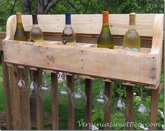 six bottles of wine are lined up in a wooden holder on a fence rail outside