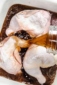 raw chicken being poured into a large pot with brown liquid in it and on top of other ingredients