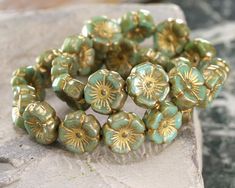 a bunch of green and gold beads sitting on top of a stone slab next to a rock