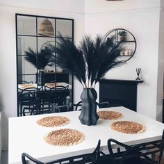 a white table topped with black chairs and a vase filled with pamodia feathers