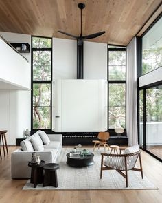 a living room with wooden ceiling and white furniture in the center, along with large windows