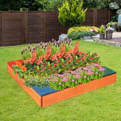 a garden filled with lots of flowers next to a lush green field and wooden fence