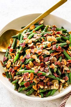 a white bowl filled with green beans and nuts next to a gold spoon on a marble surface