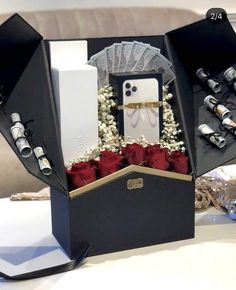 an open black box with red roses and other items in it sitting on a table