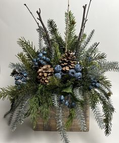 a wooden box filled with pine cones and blue berries next to greenery on a white background