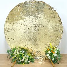 a gold sequin backdrop with flowers and greenery in front of it on a wooden floor