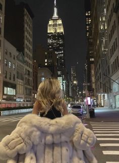 a woman is walking down the street at night with her fur coat over her shoulders