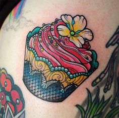 a colorful cupcake tattoo on the back of a woman's shoulder