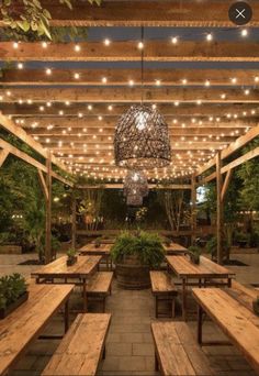 an outdoor dining area with wooden benches and lights hanging from the pergolated roof