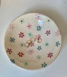 two wedding rings are placed in the center of a flowered bowl on a white surface