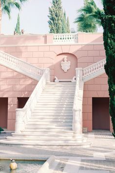 a pink building with stairs leading up to the top floor and palm trees in front of it