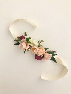 a white letter decorated with flowers and greenery on top of a plain wall surface