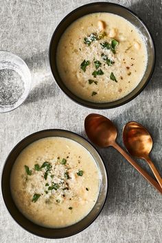 two bowls of soup with spoons next to each other on a gray tablecloth