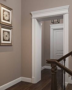 an empty hallway with framed pictures on the wall and wooden stairs leading to another room