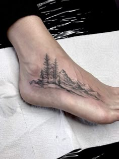 a person with a tattoo on their foot that has trees and mountains in the background