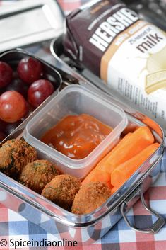 a lunch box filled with meatballs, carrots and grapes next to a can of ketchup