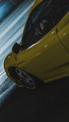 a yellow sports car parked on the side of the road at night with its door open