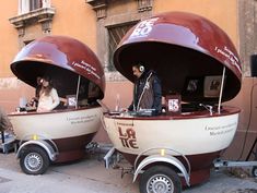 two people are sitting in the back of a boat on wheels with one person standing next to it