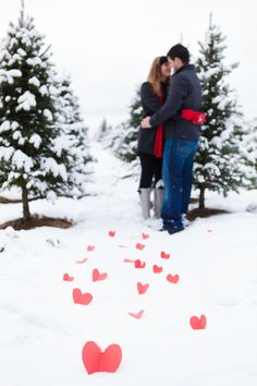 two people standing next to each other in the snow with red hearts drawn on them