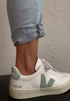 a woman's foot with a small tattoo on her left ankle and white sneakers