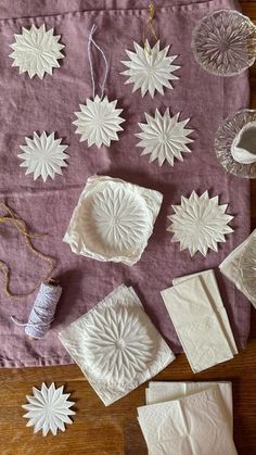 white paper snowflakes are laid out on a purple tablecloth with twine spools