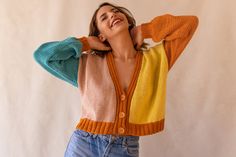 a woman is laughing while wearing a colorful cardigan sweater and denim shorts with her hands behind her head