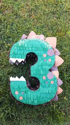 a green and pink paper mache shaped like a number three with spikes on it