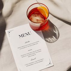 a menu sitting on top of a table next to a glass filled with ice and an orange slice