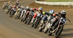 a group of motorcyclists riding down a race track with their bikes lined up