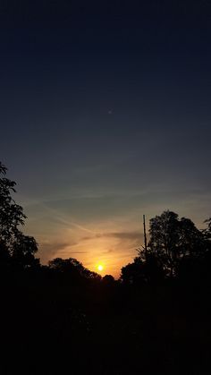 the sun is setting behind some trees in the dark sky, with only one cloud visible