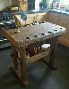 an old wooden table with plates and pans on it in the middle of a kitchen