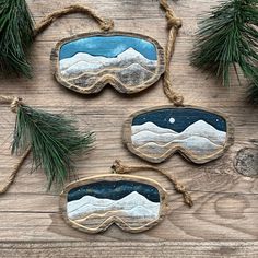 three snow goggles hanging from twine on wooden planks with pine branches and evergreen needles