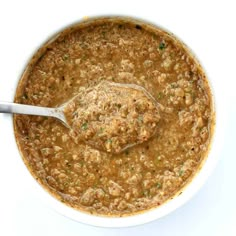 a white bowl filled with soup on top of a table next to a silver spoon