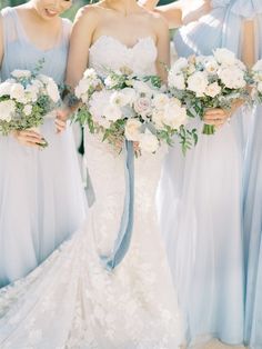 four bridesmaids in blue dresses holding bouquets with white flowers and greenery