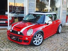 a red and white mini cooper parked in front of a building with two cars behind it